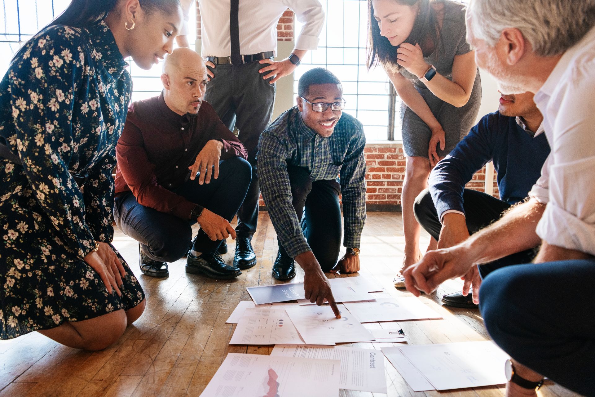 Diverse creative business team kneeling on floor around plans