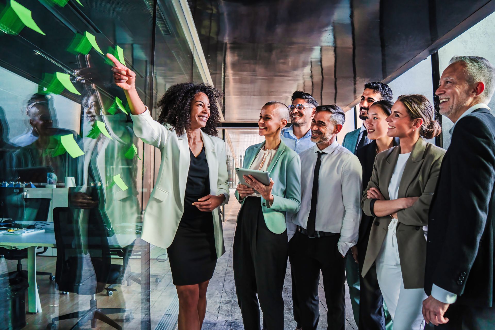 Team happily looks on as businesswoman points to post-its on glass wall