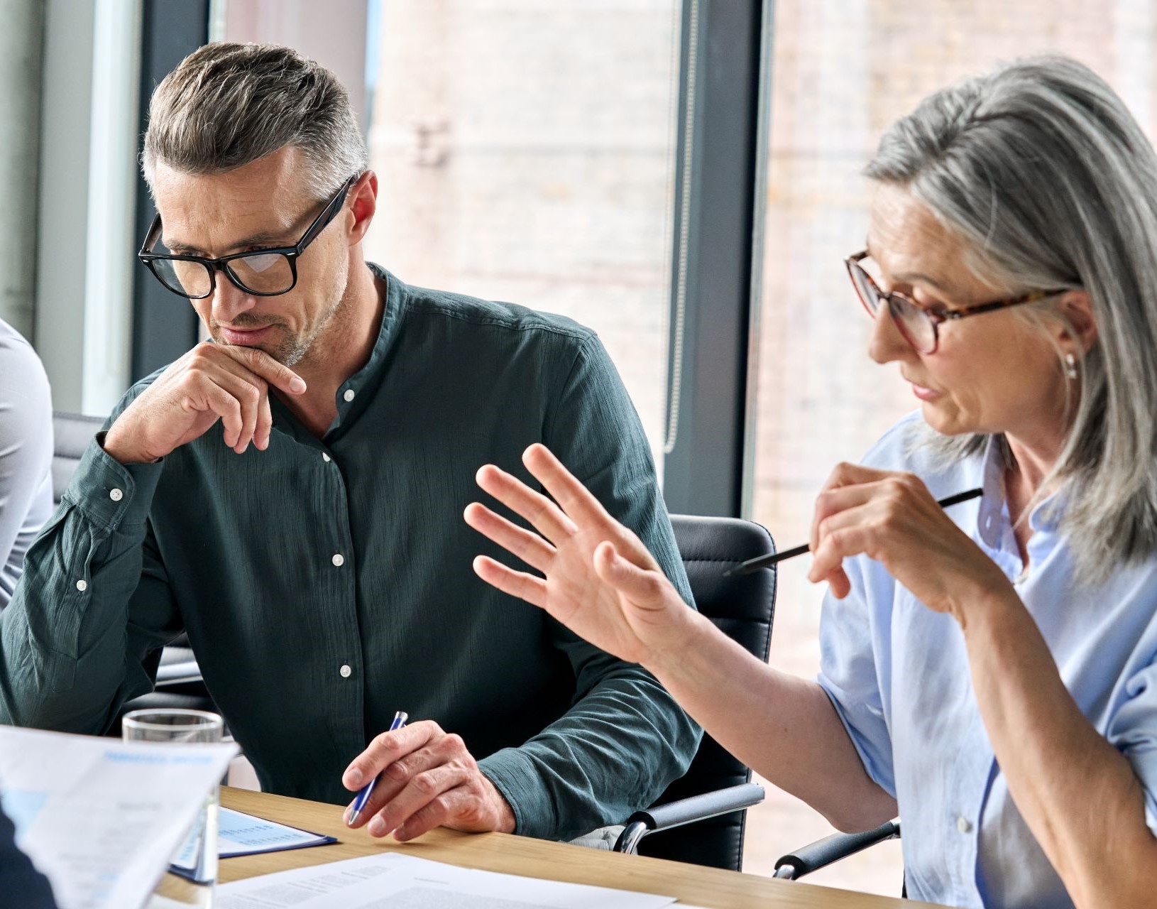 Serious mature caucasian male ceo executive manager with male business partner discussing corporation merge plan at board room table. Professional coworkers leaders doing paperwork in modern office.